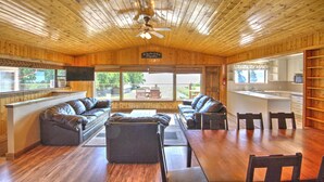 A spacious living room with a wooden ceiling, leather sofas, a dining table, and a kitchen area visible through an open doorway. - Lake-front Cabin Located In The Heart Of Bear Lake! (Garden City)