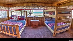 A cabin with a wooden interior, a bunk bed, a desk with a lamp, and a window with a view of the outdoors. - Lake-front Cabin Located In The Heart Of Bear Lake! (Garden City)