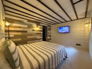 Une chambre à coucher avec un lit, un lambris en bois, un téléviseur et un plafond avec des poutres apparentes.