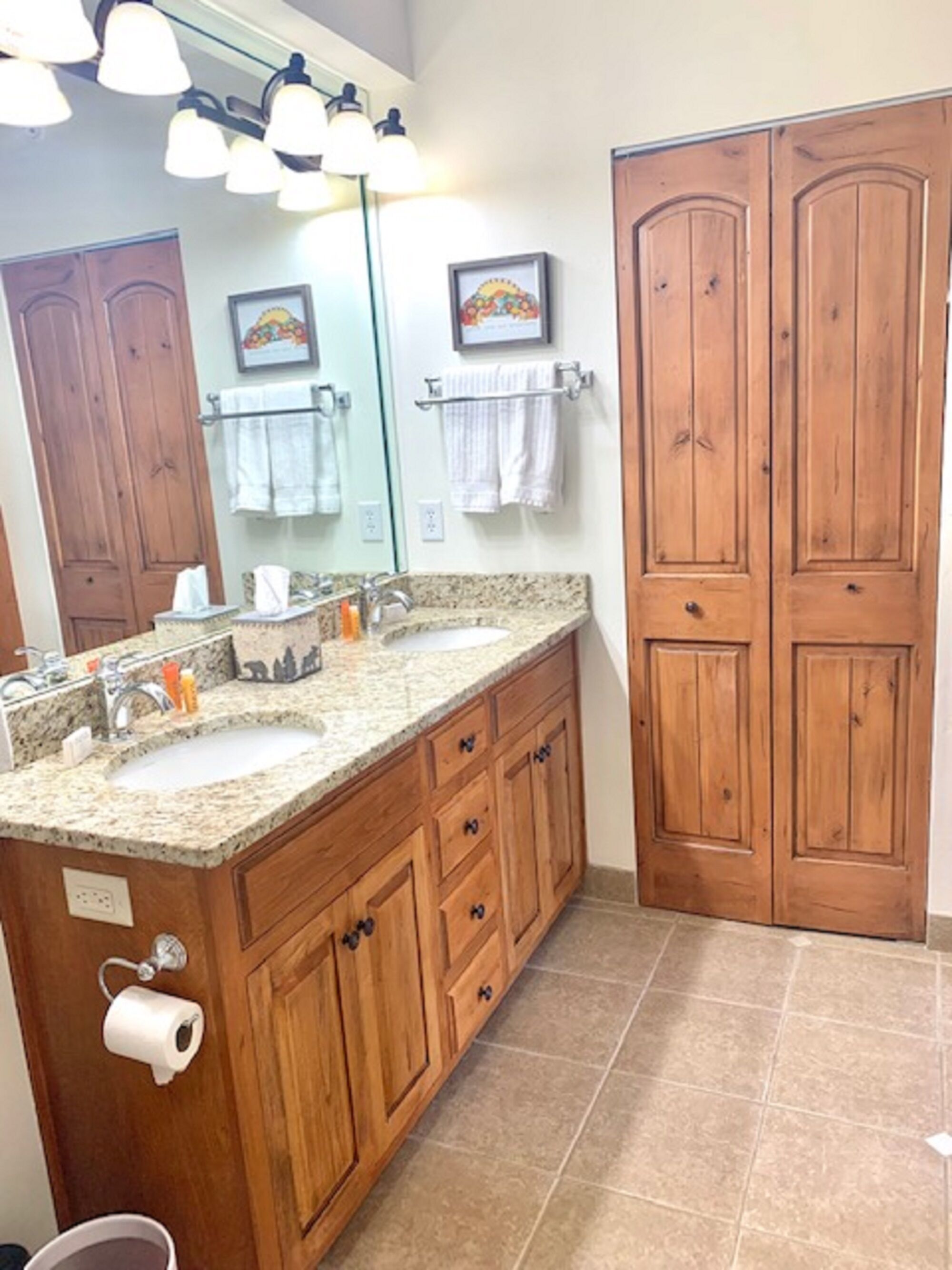 Un baño con armarios de madera, encimera de granito, lavamanos, espejo y perchero para toallas.