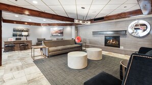 Een moderne woonkamer met een open haard, een bank, twee ronde voetenbankjes en een receptiebalie met barstoelen.