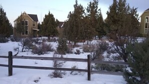 Zona residencial con suelo cubierto de nieve, valla de madera y casas con ventanas y puertas visibles.