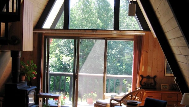 Een gezellige zolderkamer met een groot raam, houten balken, een klein keukentje en een zithoek met vloerkleed.
