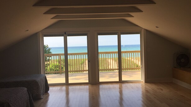 Ein geräumiges Zimmer mit einer großen Glasschiebetür, die auf einen Balkon mit Blick auf einen Strand führt.