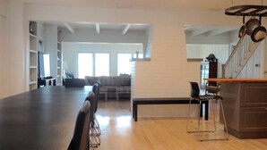 Eine geräumige Küche mit einer langen Arbeitsplatte, ein Essbereich mit Stühlen, eine Treppe und ein Wohnzimmer mit Sofa und Fernseher.