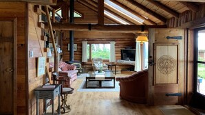 Interior de uma cabana de tronco com lareira, móveis de madeira e uma televisão.