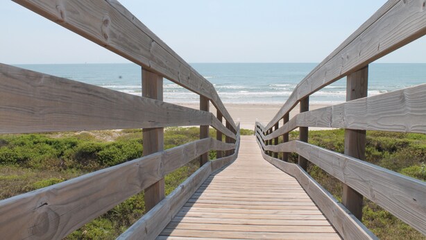 A wooden boardwalk leading to a beach with a clear view of the ocean.