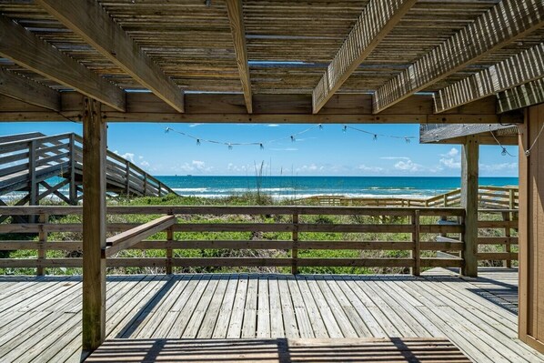 A wooden deck with a view of the ocean, a wooden railing, and a wooden staircase.