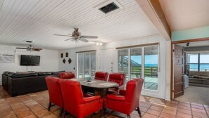 A spacious living area with a round table and red chairs, a black leather sofa, and a television.
