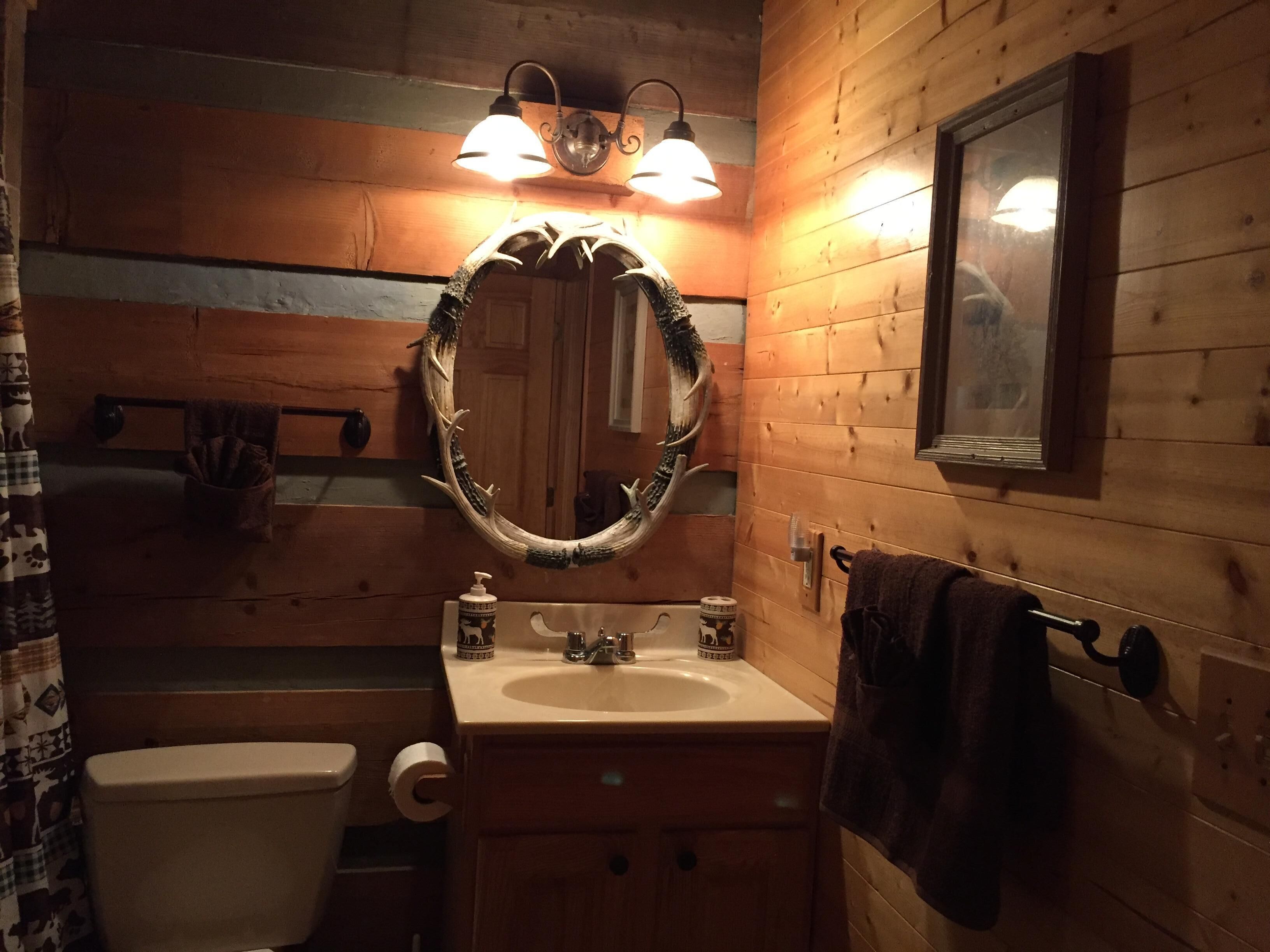 Ein Badezimmer einer Holzhütte mit Waschbecken, Toilette und Spiegel mit Dekoration aus einem Hirschgeweih.