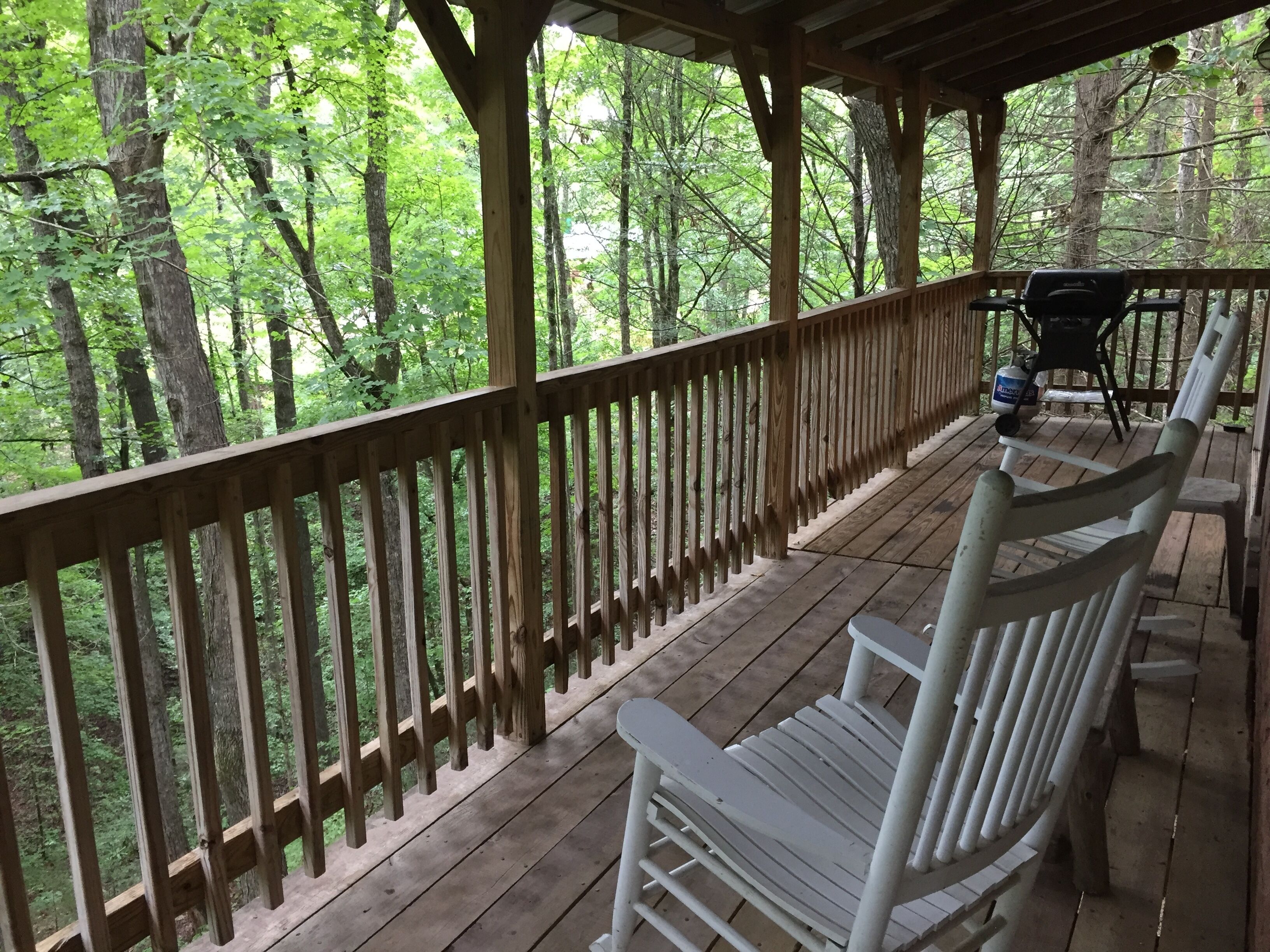 A wooden deck with a railing, a white bench, and a grill area.