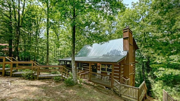 A rustic cabin with a metal roof, wooden deck, and a small porch.