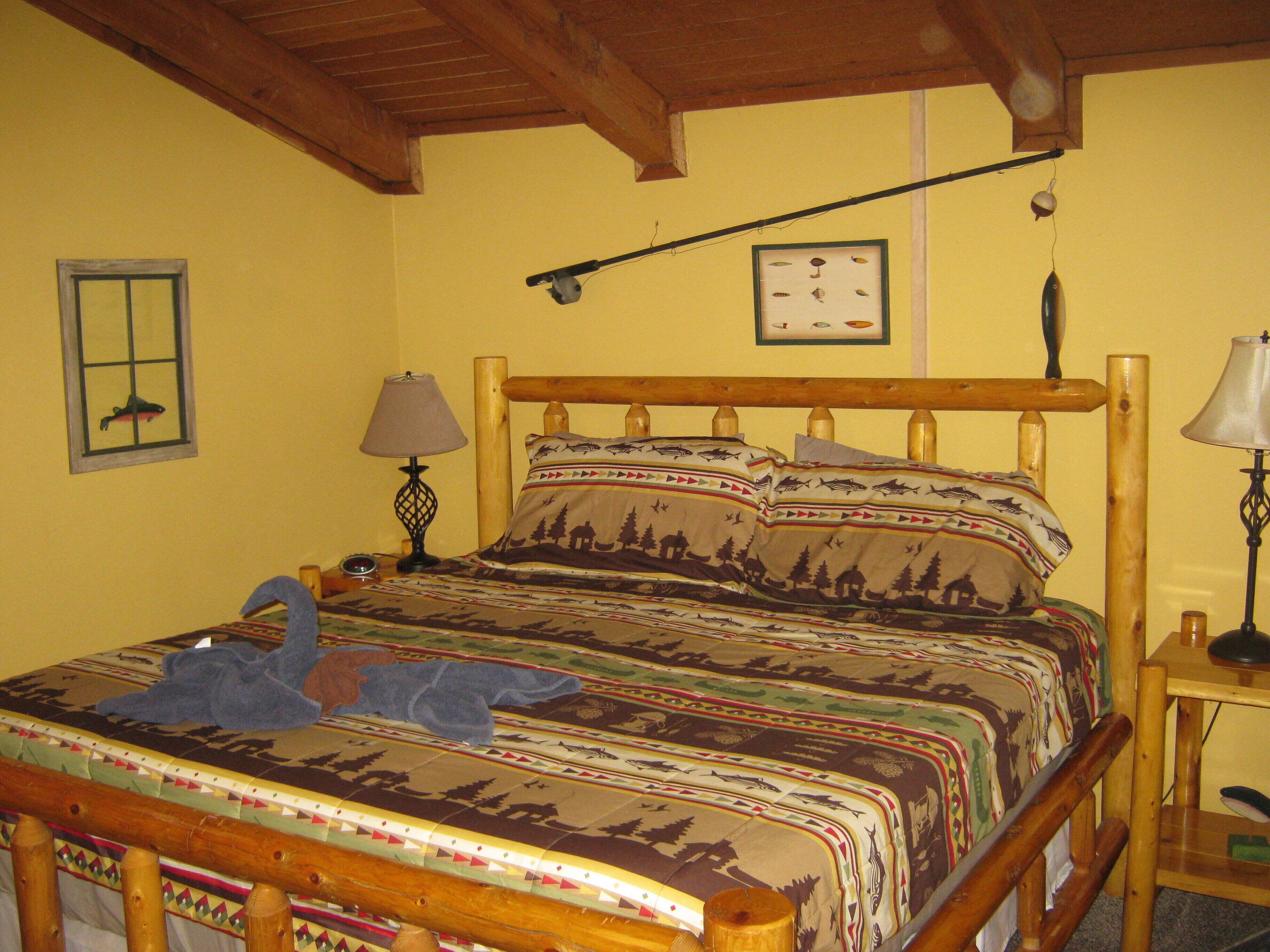 A bed with a wooden frame and a colorful bedspread featuring animal prints. There is a small table with a lamp beside the bed.