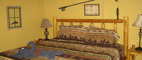 A bed with a wooden frame and a colorful bedspread featuring animal prints. There is a small table with a lamp beside the bed.