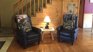 A wooden staircase with a handrail, two armchairs with patterned cushions, a small table with a lamp, and a framed picture on the wall.