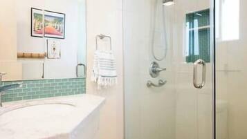 Un baño con cabina de ducha de vidrio, un lavamanos con encimera de mármol y un perchero para toallas.