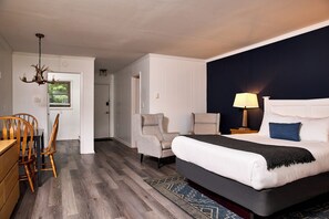A hotel room with a bed, two armchairs, a dining table with chairs, a chandelier, and a nightstand with a lamp. - Catskill Seasons Inn (Shandaken)