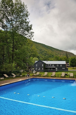 A swimming pool with lounge chairs and a building in the background. - Catskill Seasons Inn (Shandaken)