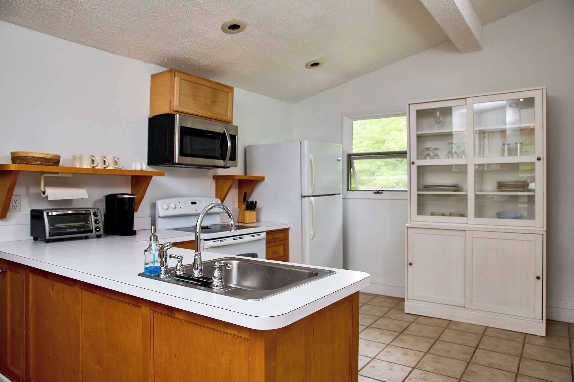 A compact kitchen with a central island, a microwave, a stove, a refrigerator, and a cabinet with glass doors.