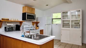 A compact kitchen with a central island, a microwave, a stove, a refrigerator, and a cabinet with glass doors.