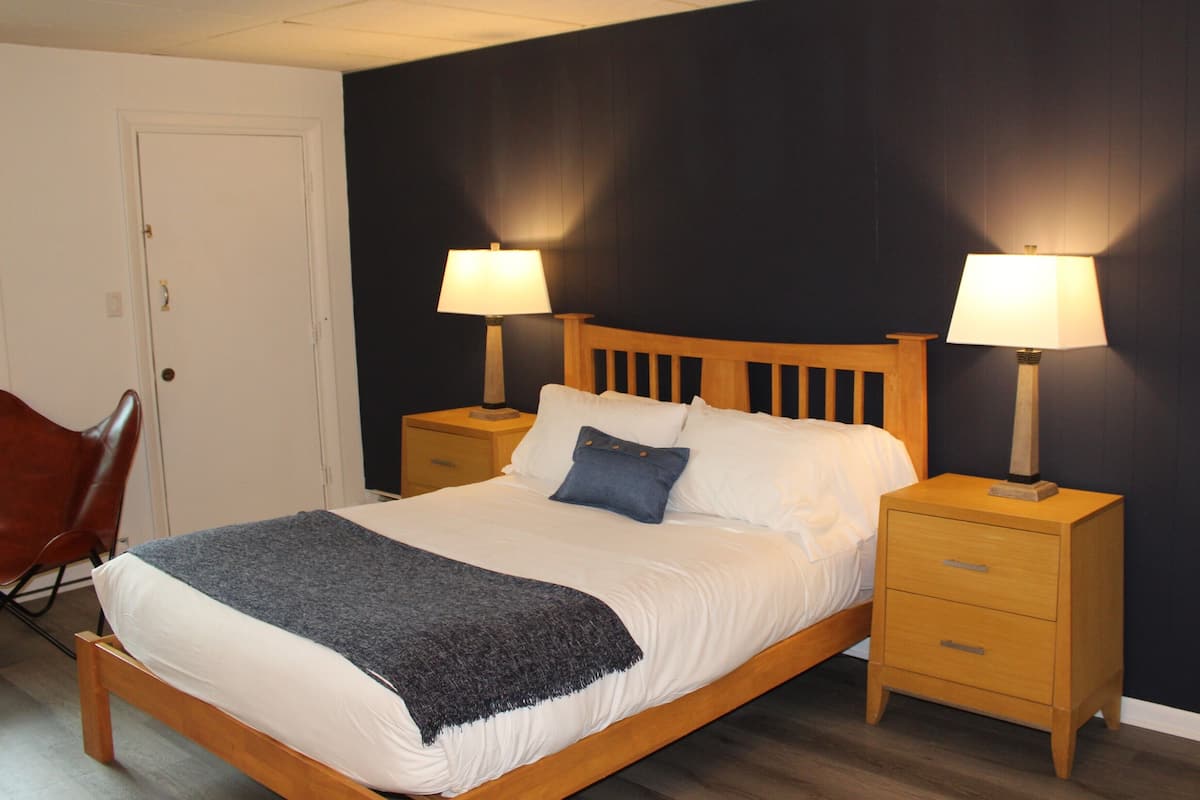 A neatly made bed with a blue pillow, two bedside tables with lamps, a wooden headboard, and a chair.