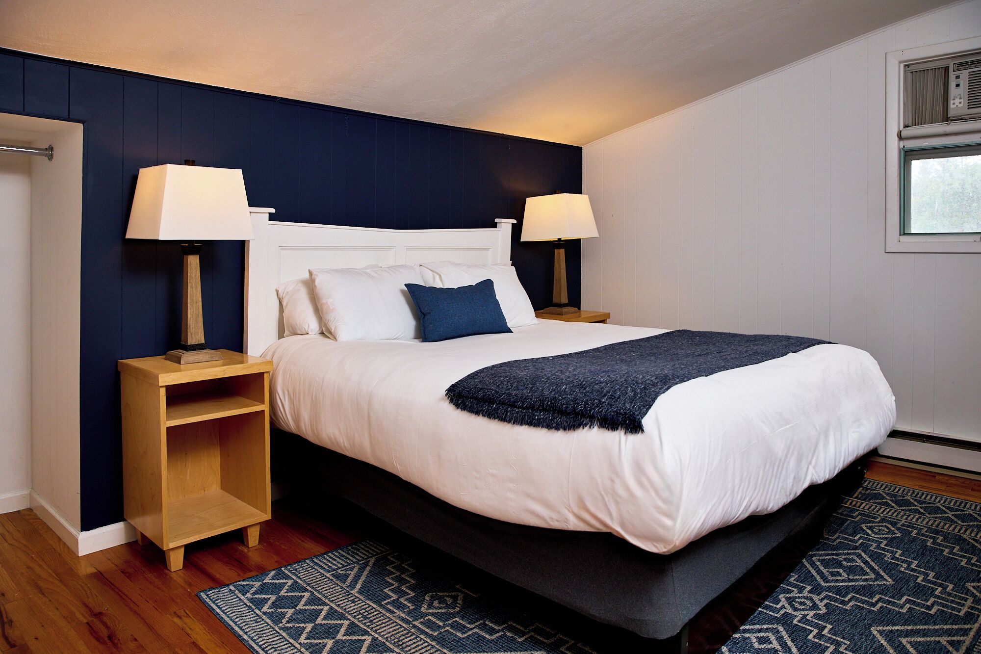A neatly made bed with a white headboard, two bedside lamps, and a dark blue throw blanket.