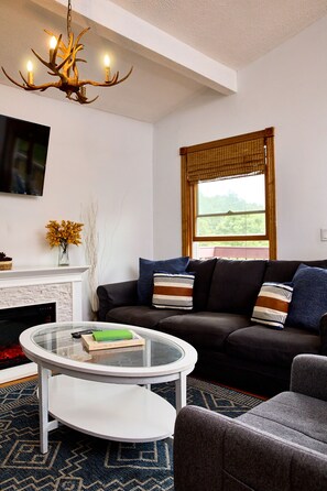 A modern living room with a fireplace, a sofa, a glass coffee table, and a television mounted on the wall.