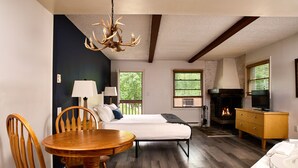 A room with a bed, a wooden dining table, chairs, a chandelier, a fireplace, and a television.