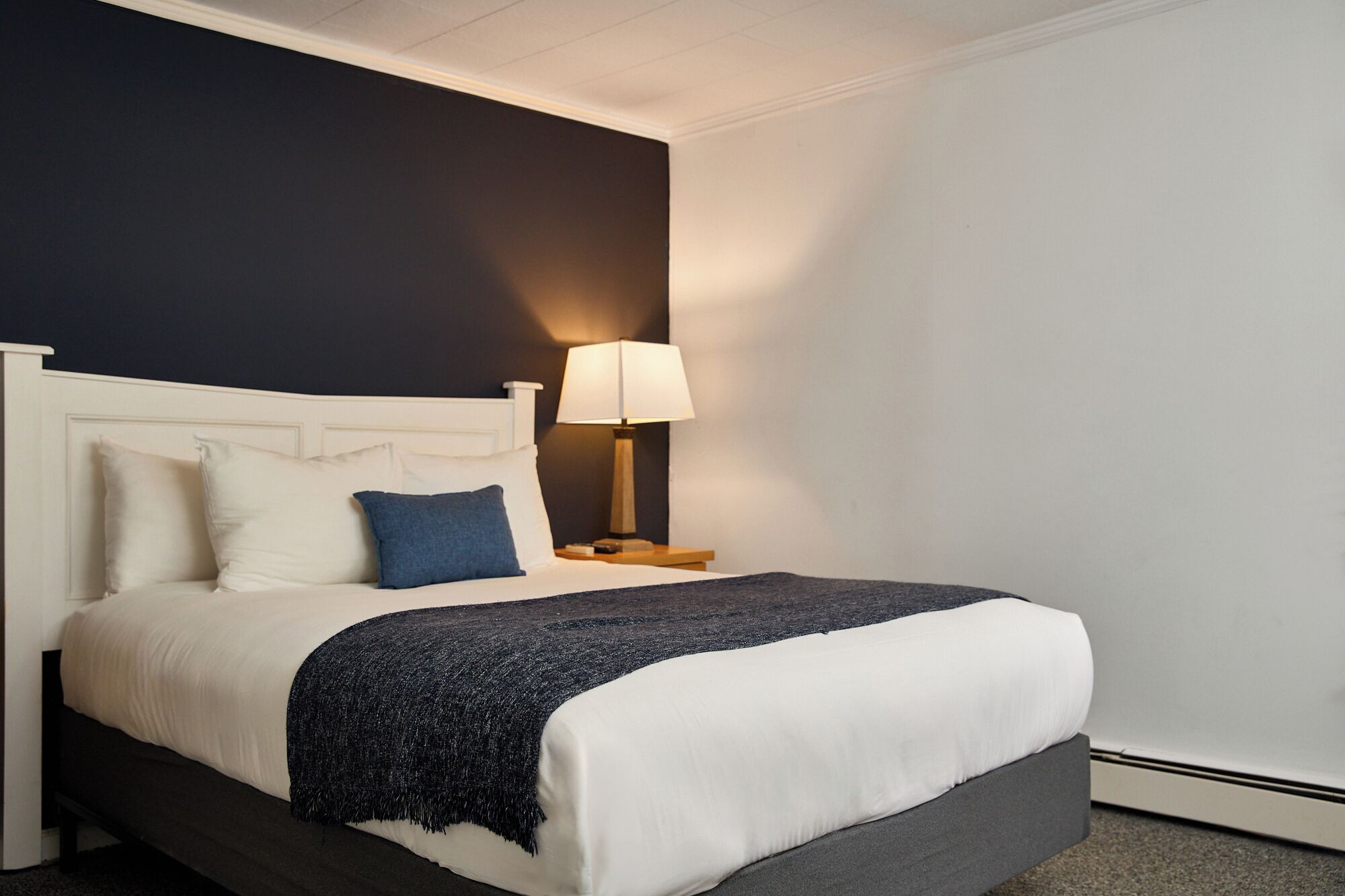 Una cama con cabecera blanca, manta azul oscuro y almohada blanca.