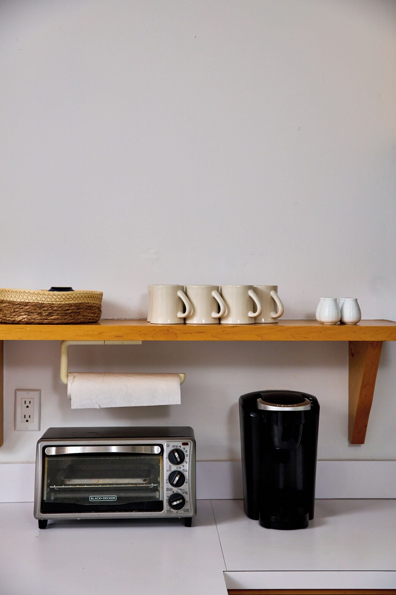 A kitchen with a wooden shelf holding mugs and a toaster oven.