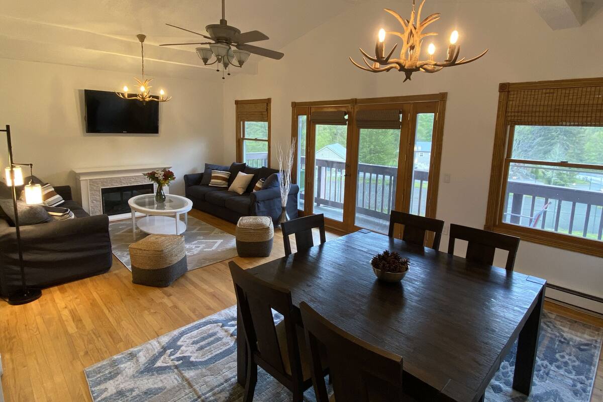 A spacious living area with a fireplace, a dining table with chairs, a sofa, and a ceiling fan.