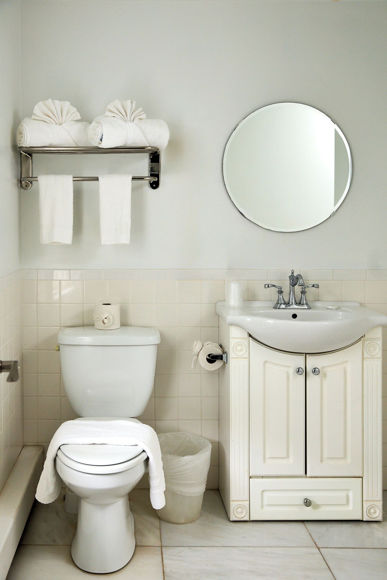A bathroom with a toilet, sink, mirror, and towel rack.
