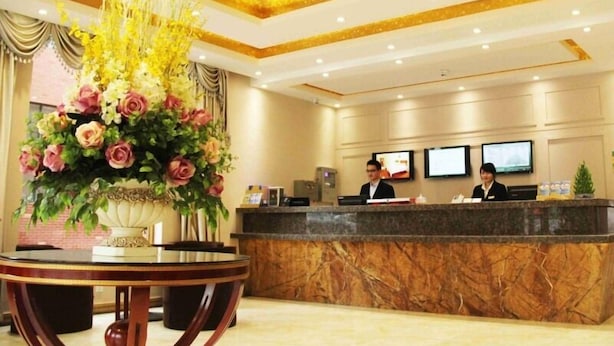 A hotel reception area with a marble reception desk, two receptionists, and a large floral arrangement. - GreenTree Inn Qingdao Development District SDUST Express Hotel (Qingdao)