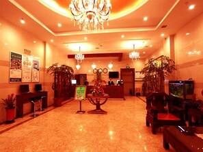 A hotel lobby with a reception desk, a chandelier, potted plants, and a fish tank.