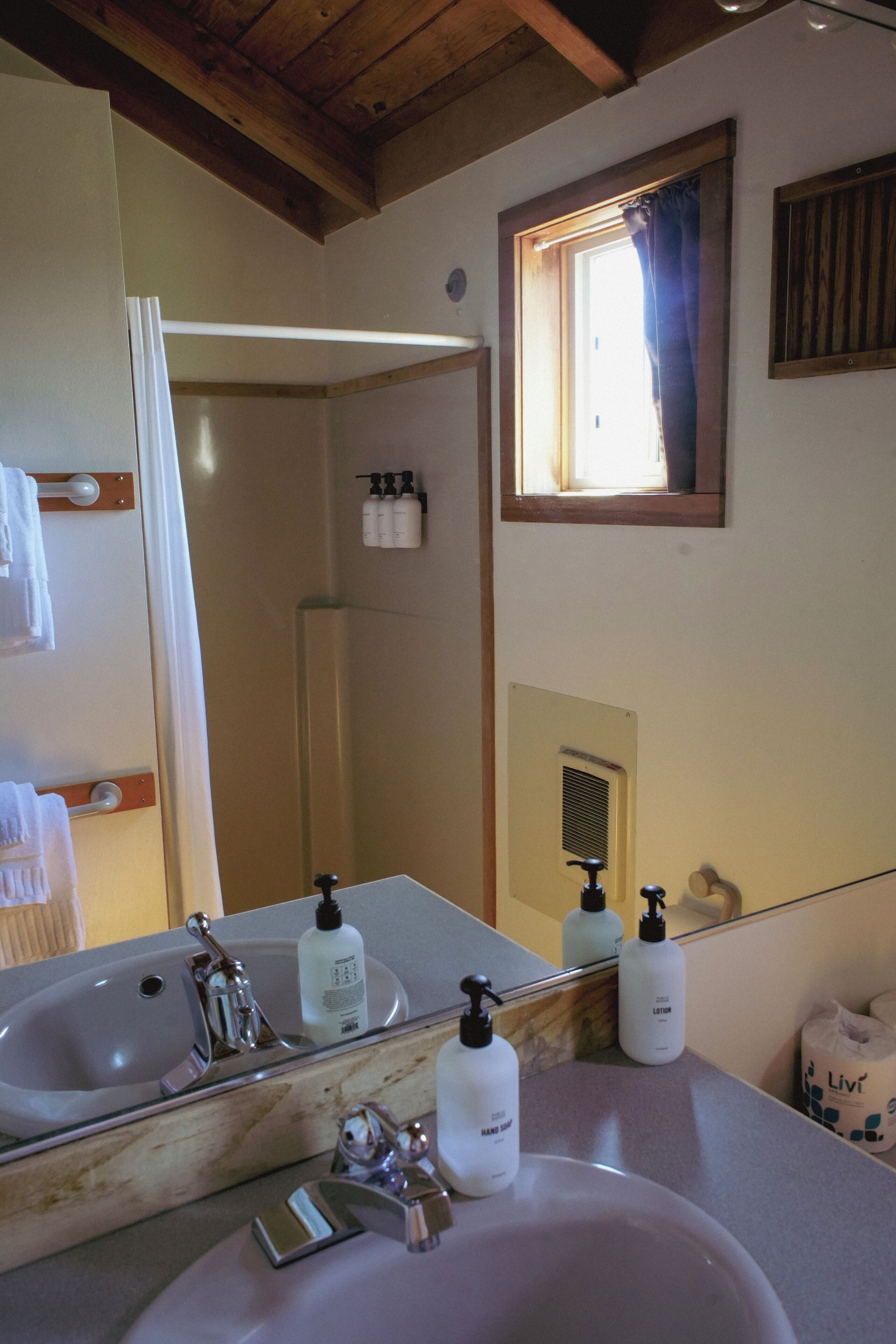 A bathroom with a large mirror, two sinks, and a window with curtains.