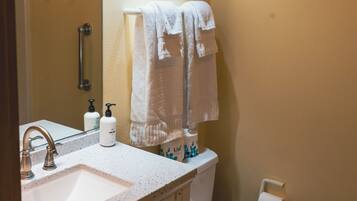A bathroom with a sink, mirror, towel rack, toilet, and a roll of toilet paper.