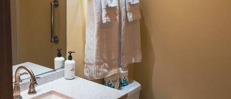 A bathroom with a sink, mirror, towel rack, toilet, and a roll of toilet paper.