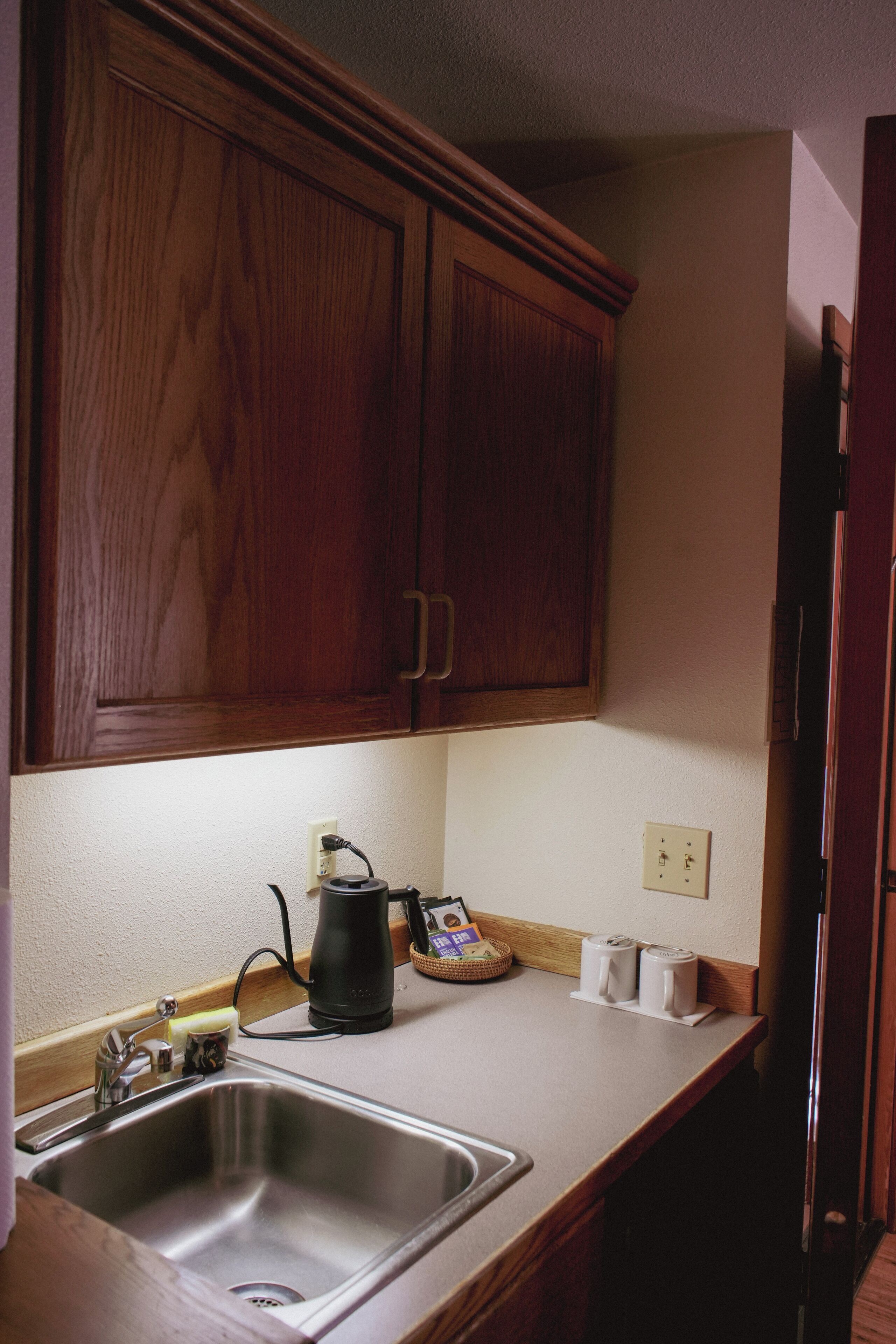 A kitchen with wooden cabinets, a stainless steel sink, a kettle, and a toaster.