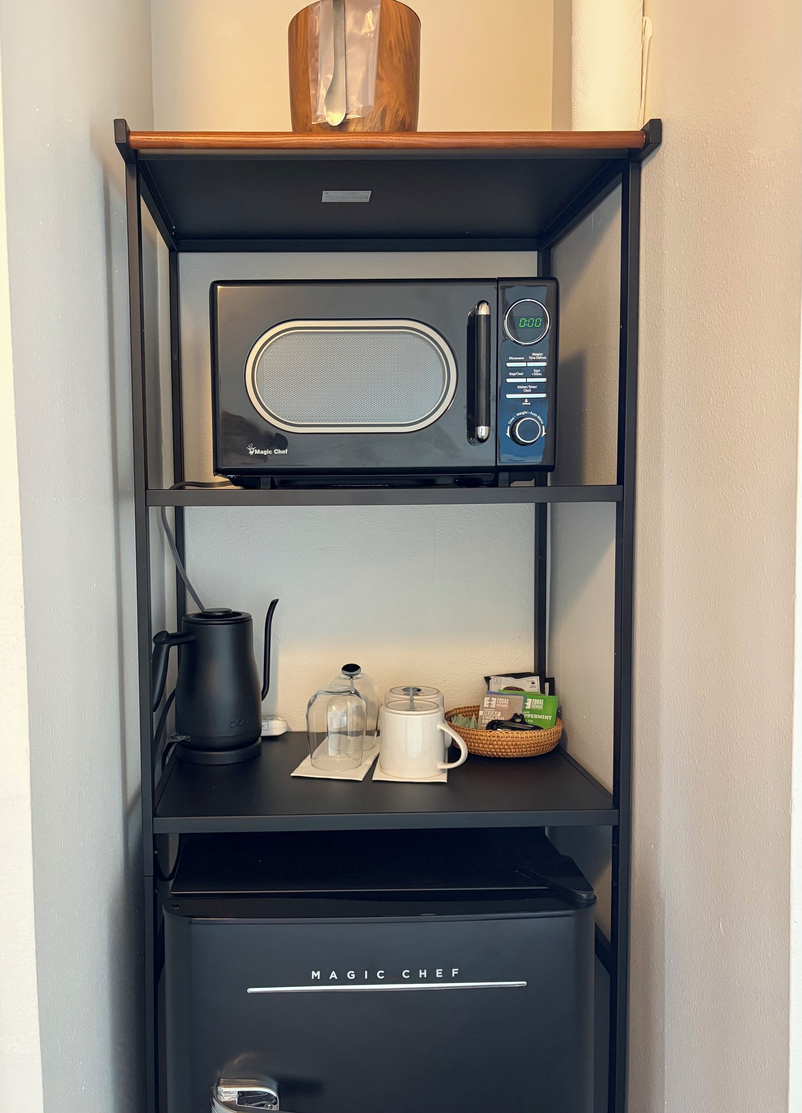 Une cuisine avec un four à micro-ondes sur l’étagère supérieure, une machine à café et un récipient en verre sur l’étagère du milieu, et une poubelle sur l’étagère inférieure.