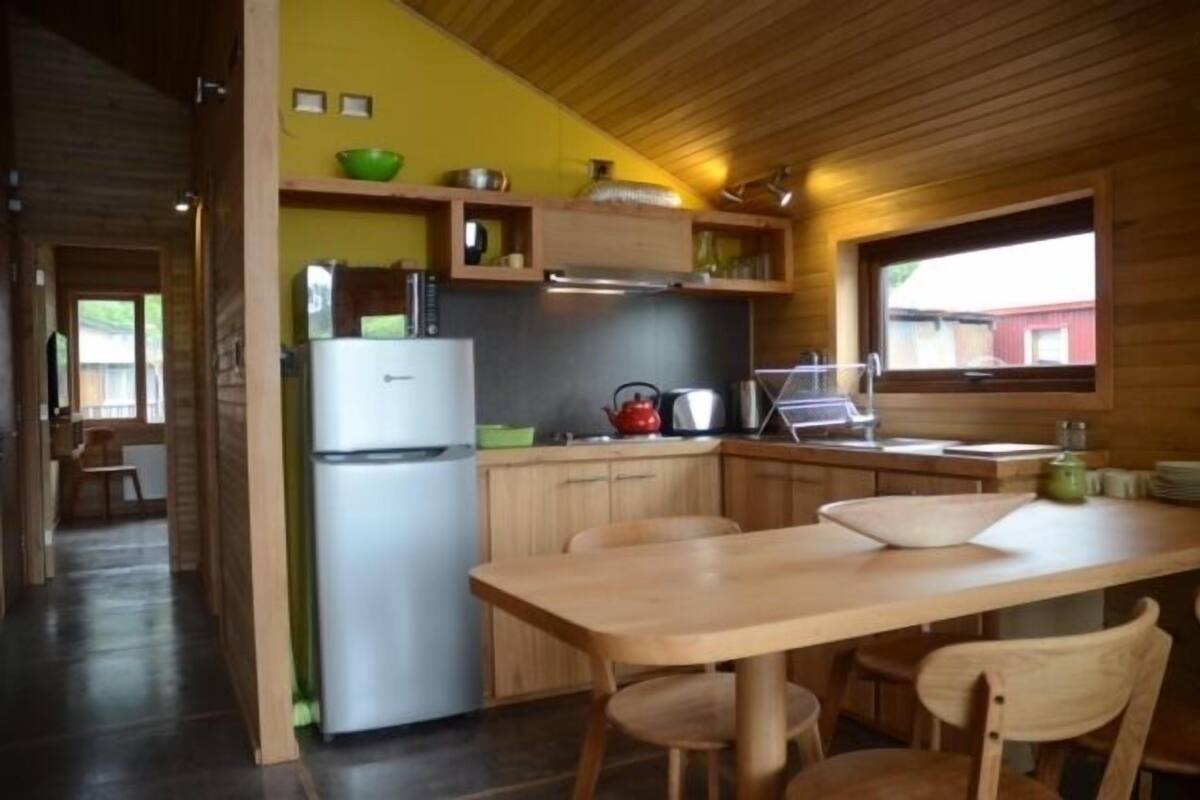 A compact kitchen with wooden cabinets, a refrigerator, a stove, and a dining area with a table and chairs.