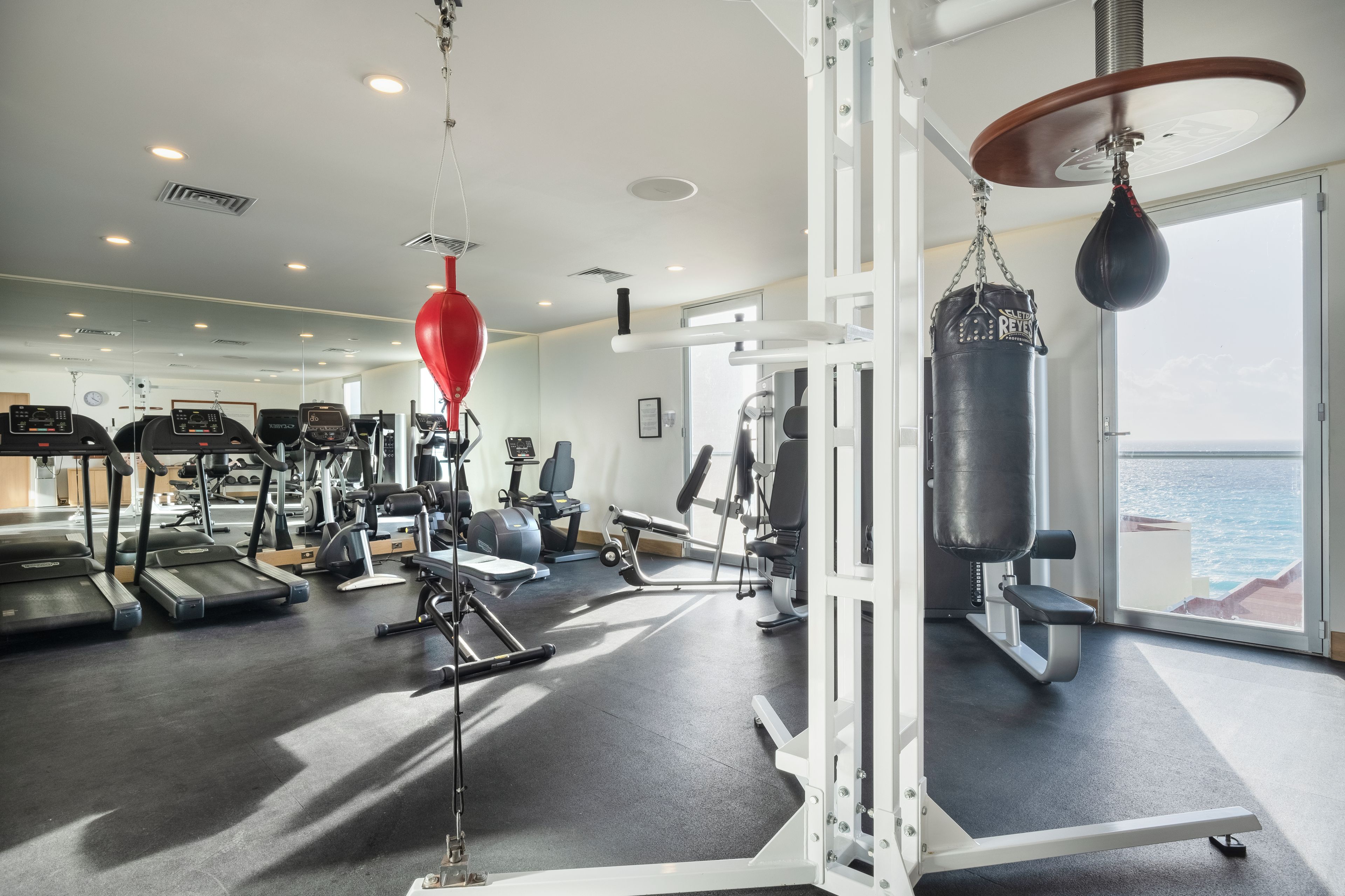 Une salle de sport équipée de divers appareils d’exercice, notamment des tapis de course, des appareils de musculation et un sac de frappe.