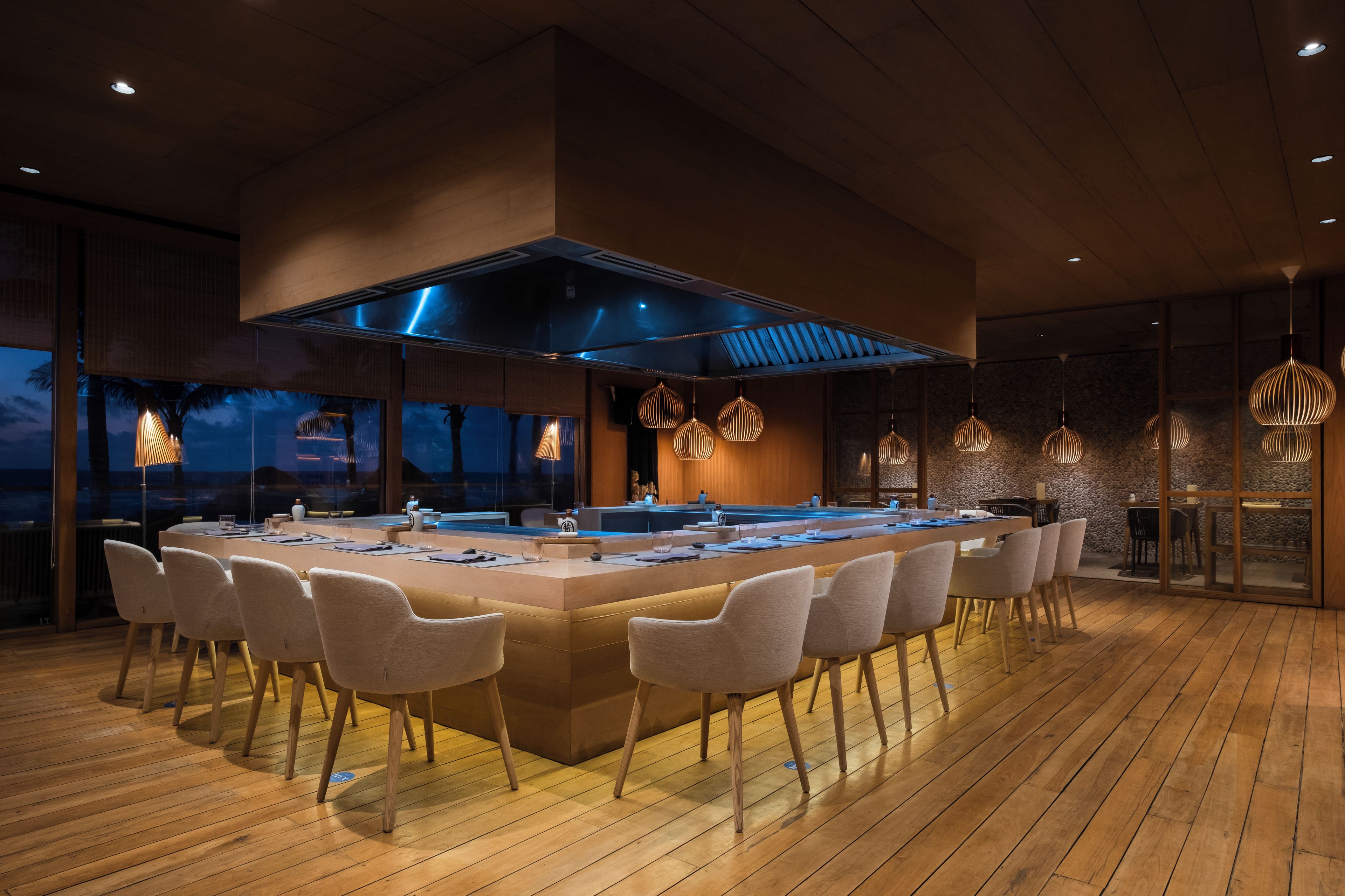 A modern kitchen with a central island, seating area, and large windows overlooking a scenic view.