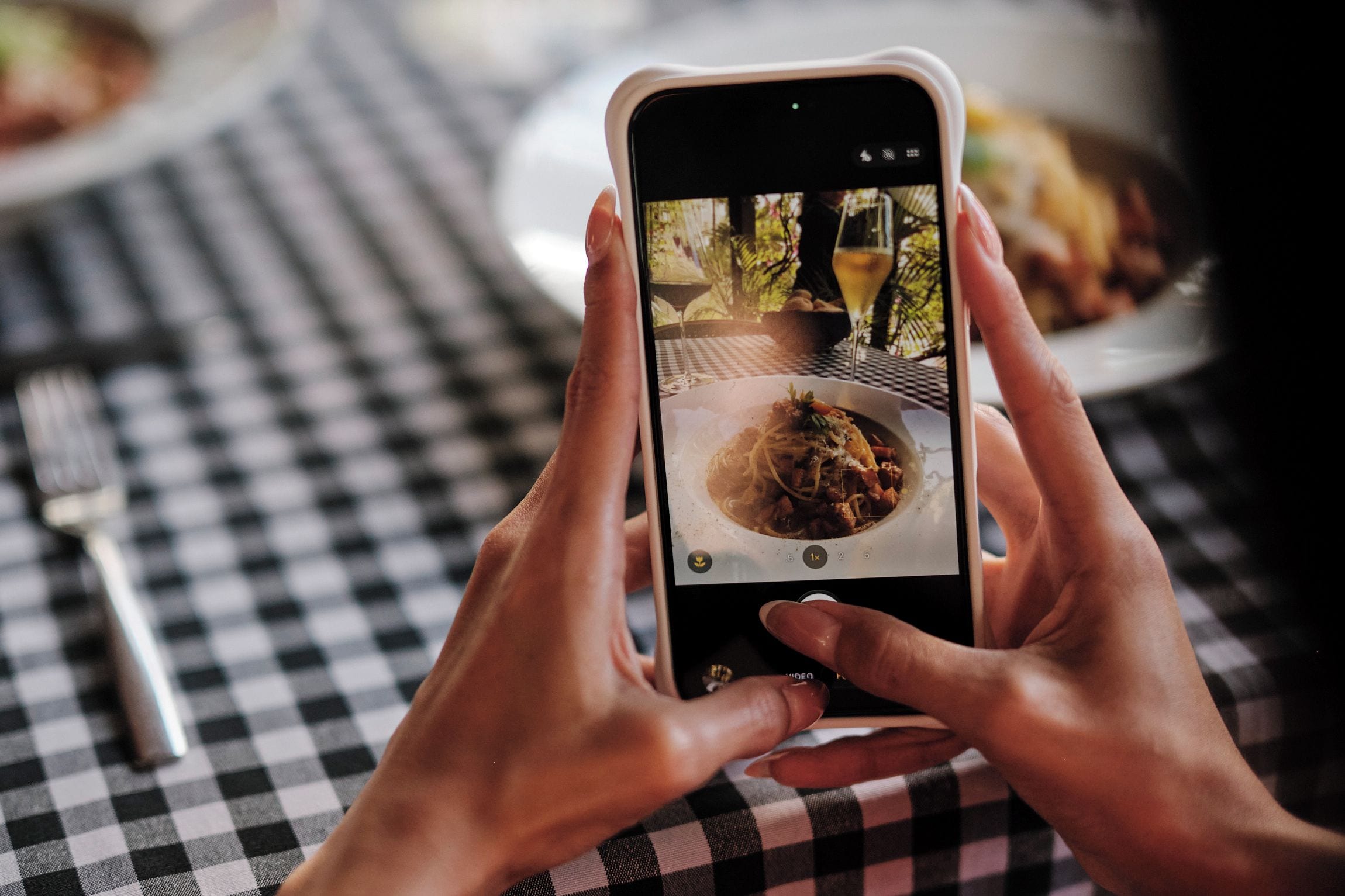 En person holder en smartphone med et billede af et måltid på et bord.