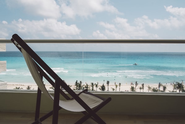 A beach view from a balcony with a wooden chair. - Hotel NYX Cancun All Inclusive (Cancun)