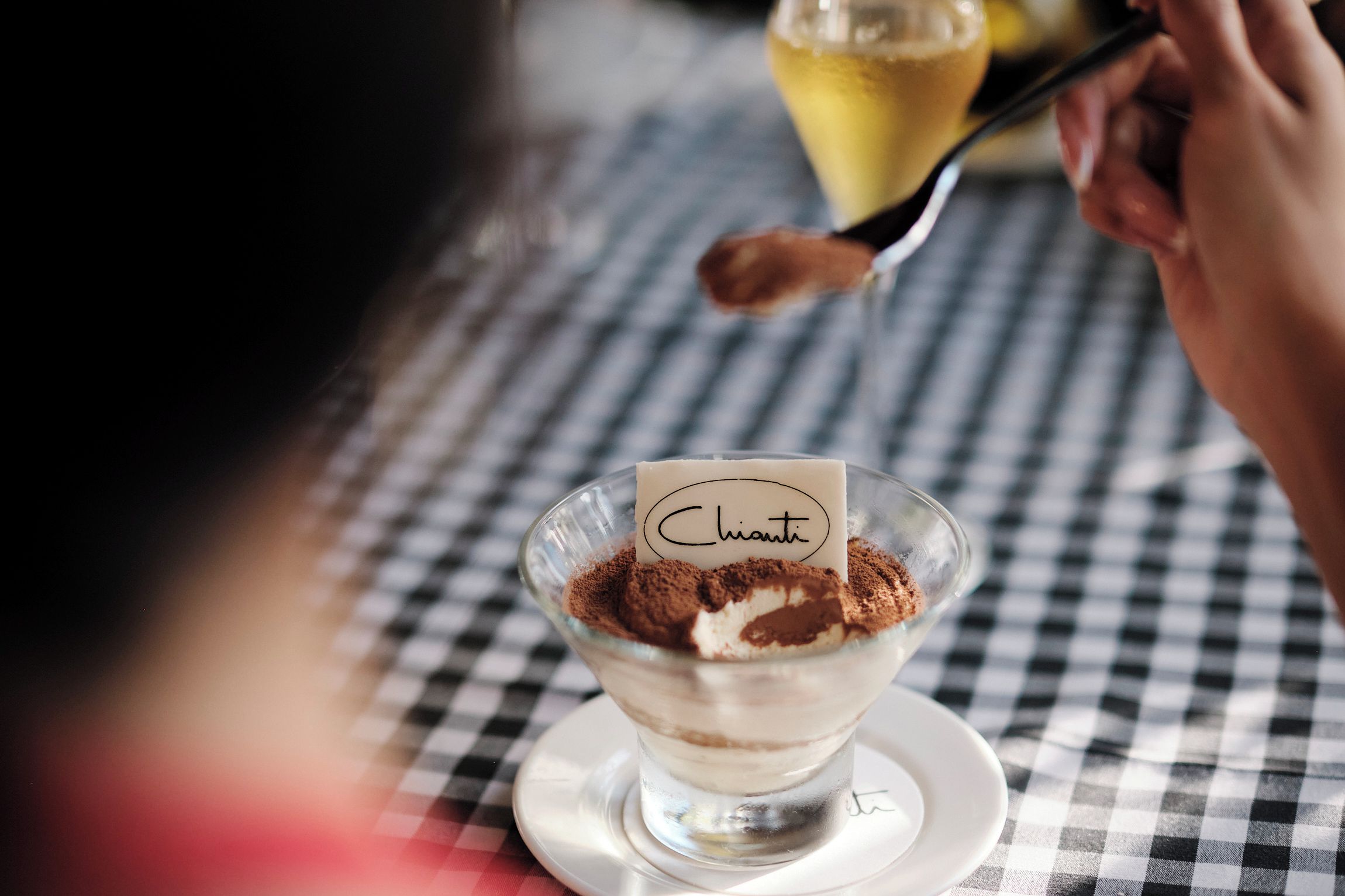 A dessert in a glass bowl with a label, placed on a checkered tablecloth.