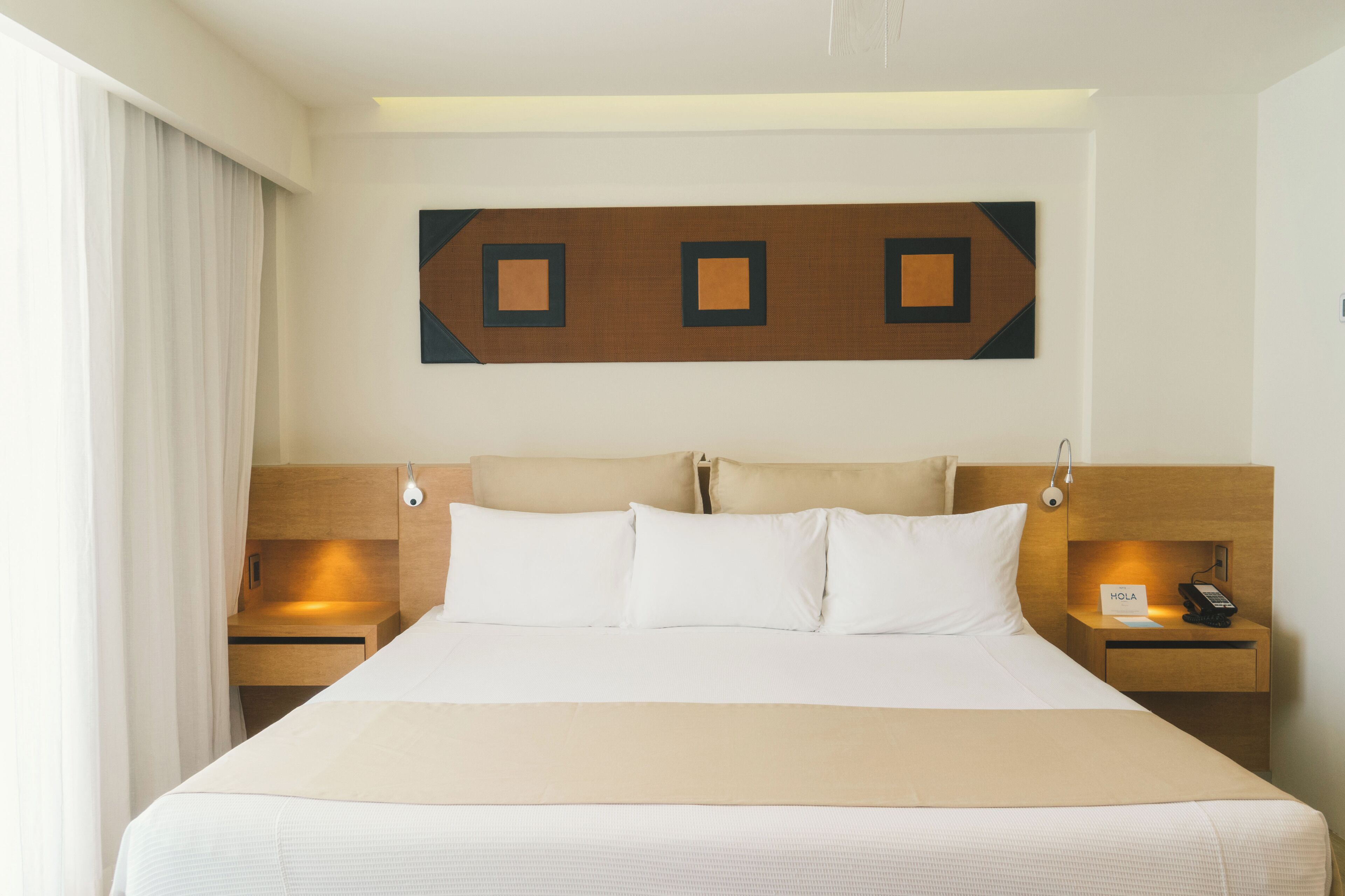 Habitación de hotel con una cama grande, dos mesitas de noche, una obra de arte colgada en la pared y una ventana con cortinas.