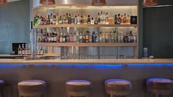 A bar area with multiple shelves of liquor bottles, a bar counter, and three cushioned stools.