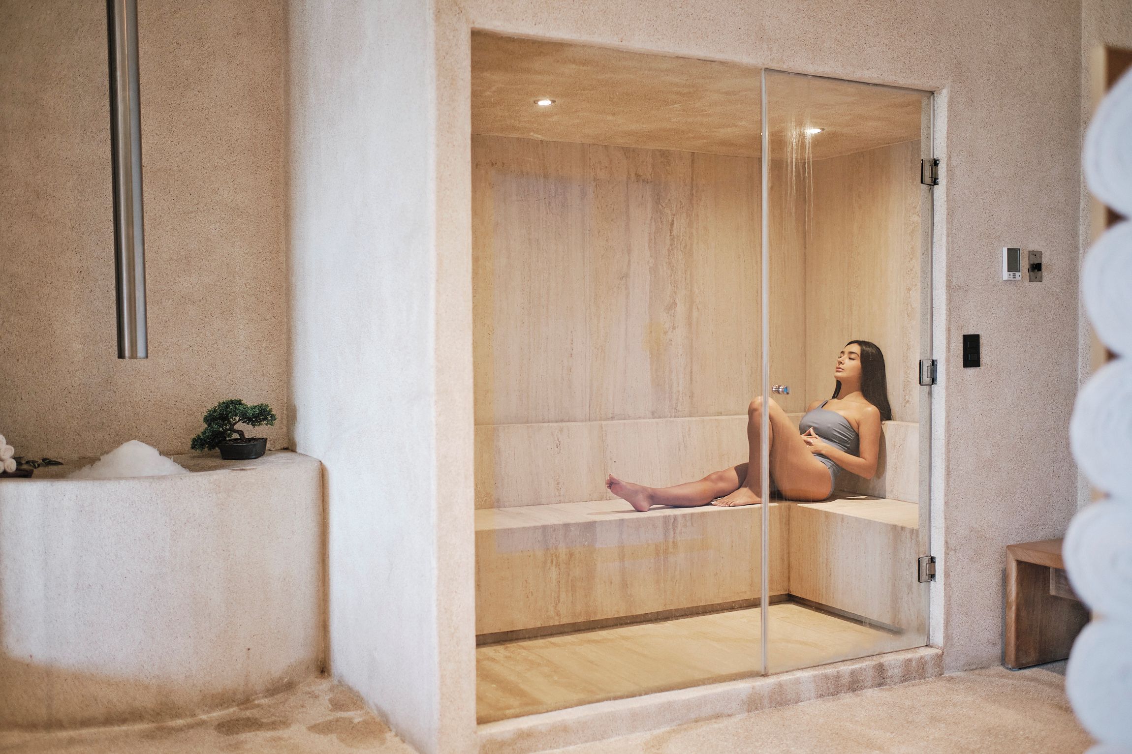 A spa room with a wooden bench, a small plant, and a glass enclosure.