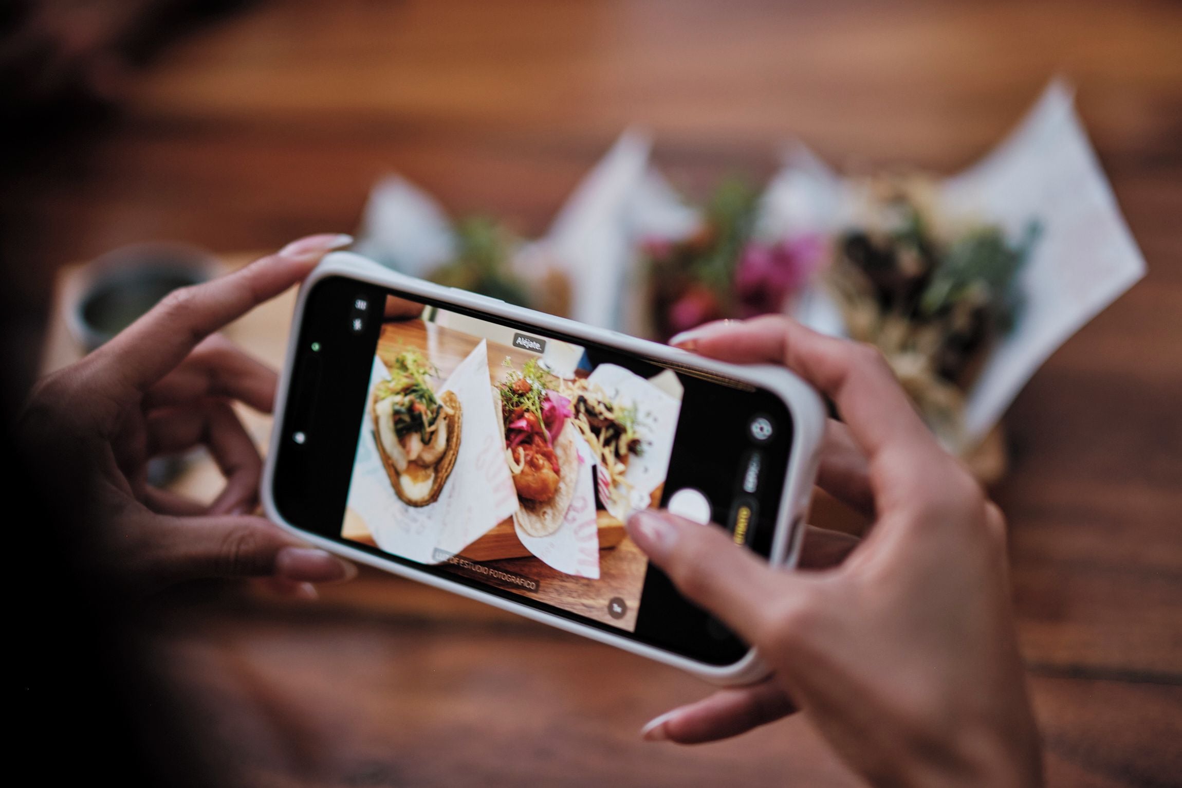 Una persona sosteniendo un teléfono inteligente, fotografiando alimentos sobre una mesa.
