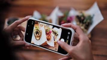 Una persona sosteniendo un teléfono inteligente, fotografiando alimentos sobre una mesa.